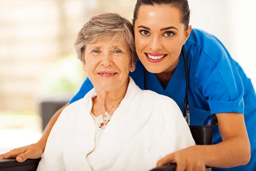 Nurse and elderly woman smiling together at the camera.