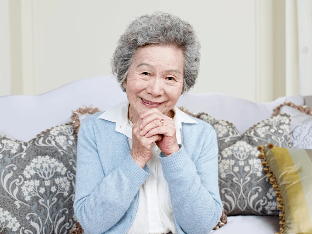 Elderly woman patient smiling at camera with her hands clasped.