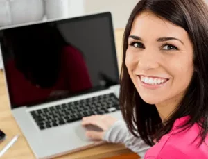 A woman smiling by her laptop.