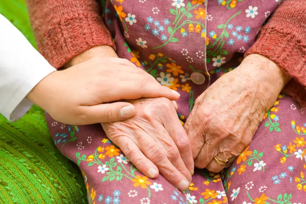 A woman holding an elderly woman's hand.