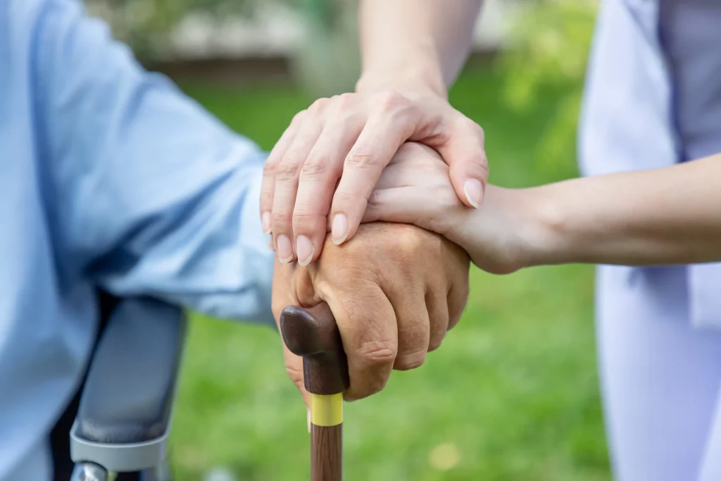 A health aide holding hands with an elderly person.