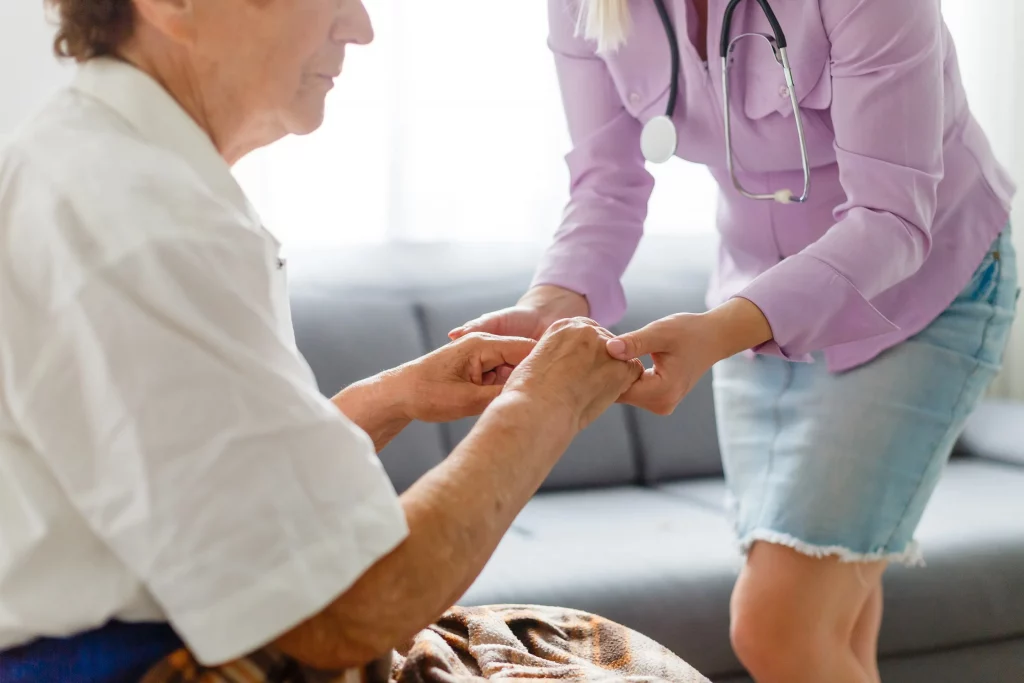 A nurse holding an elderly man's hands to help him up.