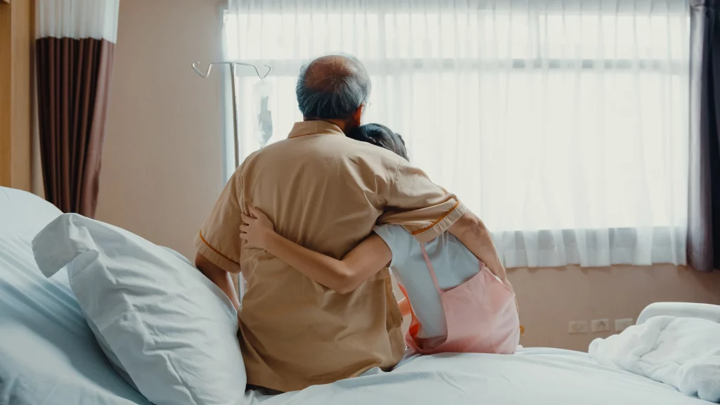 An elderly man hugging his grandchild while sitting on a bed.