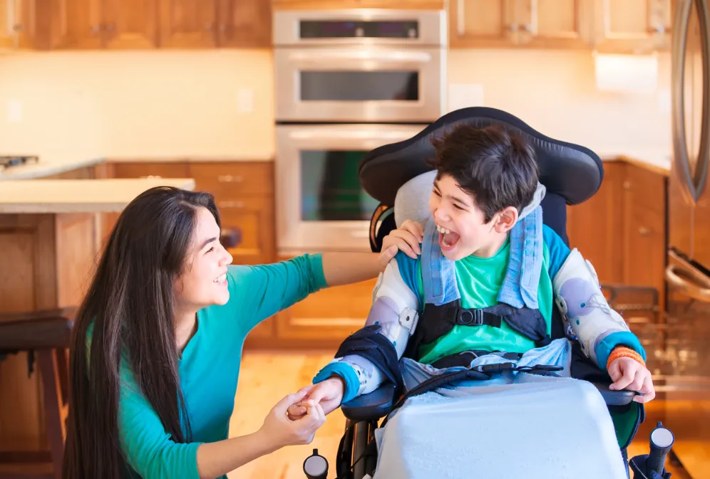 A caregiver smiling with her pediatric patient in a wheelchair.