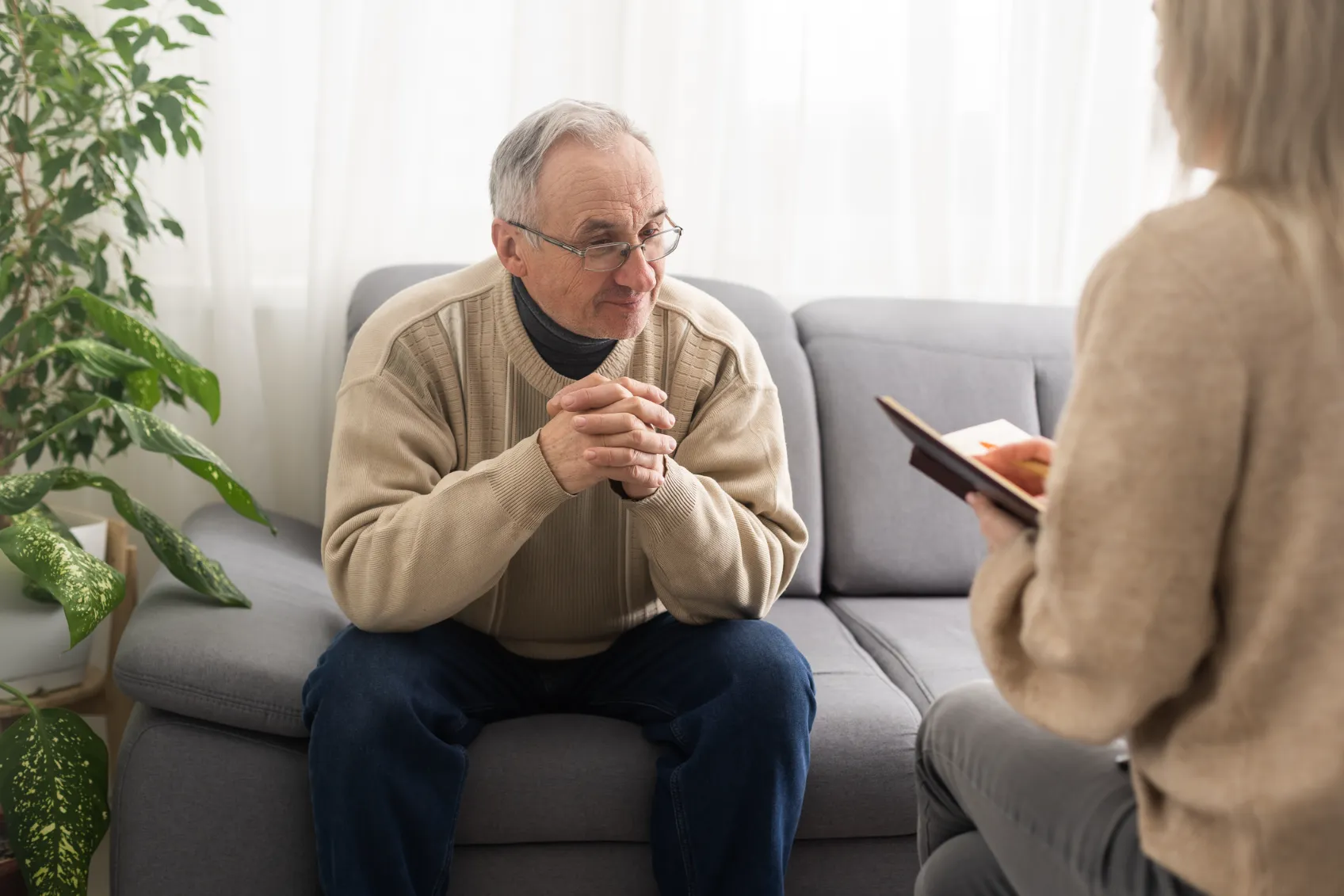 An older man sitting on a couch speaking with someone.