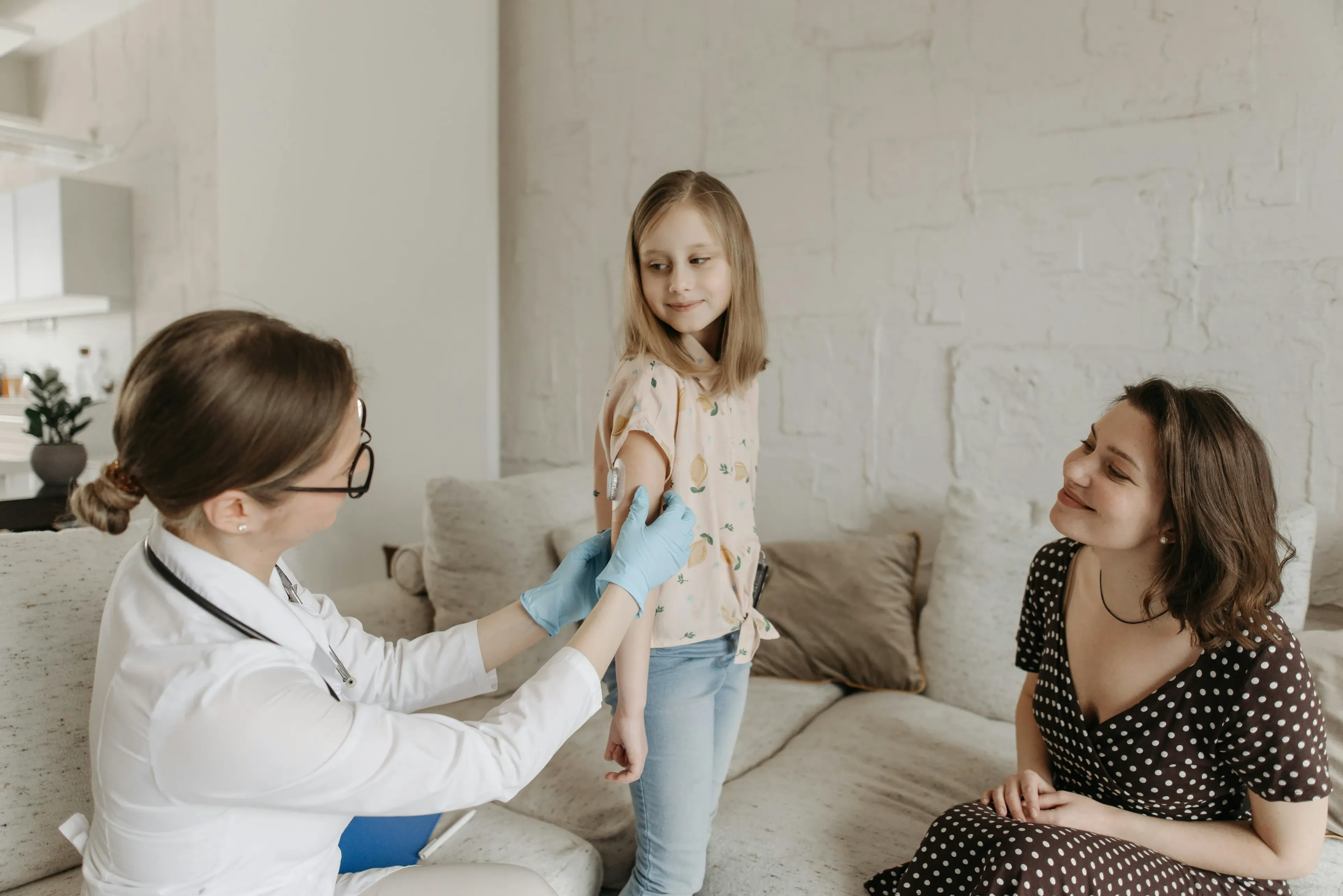 A young girl getting medical attention next to her mom in her home. 