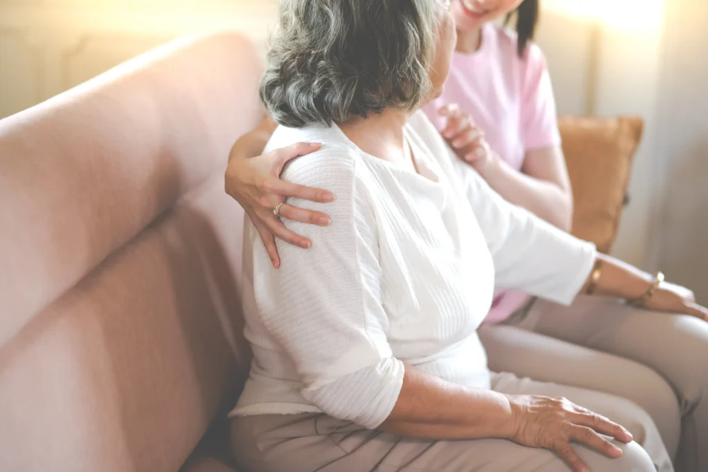 Two women sitting on the couch, one woman having her arms around the other.