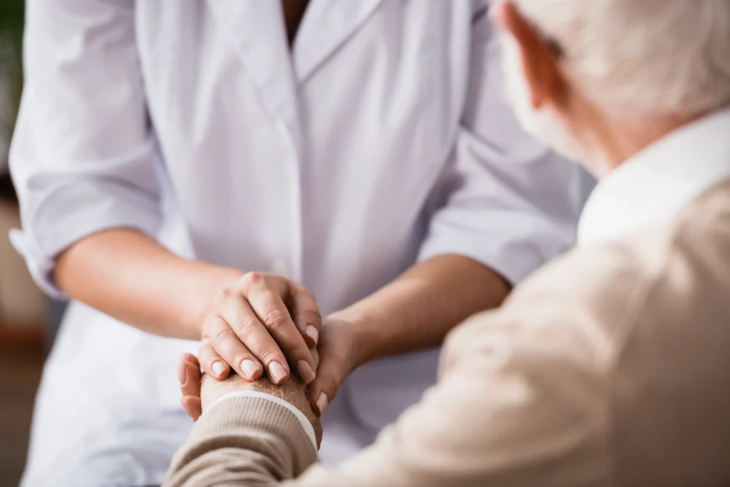 A home health aide holding the hand of an elderly patient.