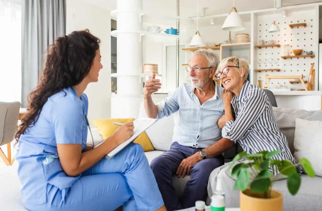 A home health aide sitting and talking to an elderly couple in their home.